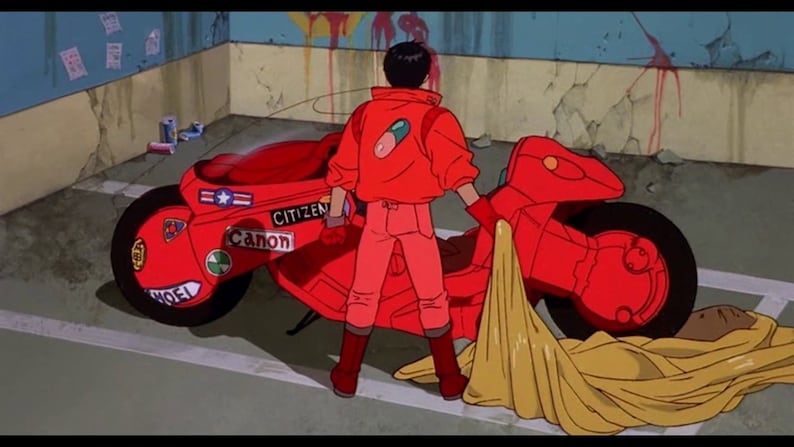 May include: A red motorcycle with a yellow tarp covering the back seat. The motorcycle has stickers on the side that say "Citizen" and "Canon". A person in a red jacket and red pants is standing next to the motorcycle.