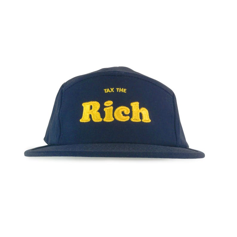 May include: Navy blue five-panel cap with a flat brim. The cap features the embroidered text "TAX THE Rich" in yellow, with the words stacked on top of each other. The hat is made of a soft material and is suitable for casual wear.