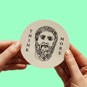 Può includere: Un adesivo rotondo bianco con un disegno a linea nera di un uomo con la barba e il testo "THINK MORE" stampato verticalmente sul lato destro.