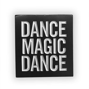 May include: Black square pin with white raised lettering that reads "DANCE MAGIC DANCE".