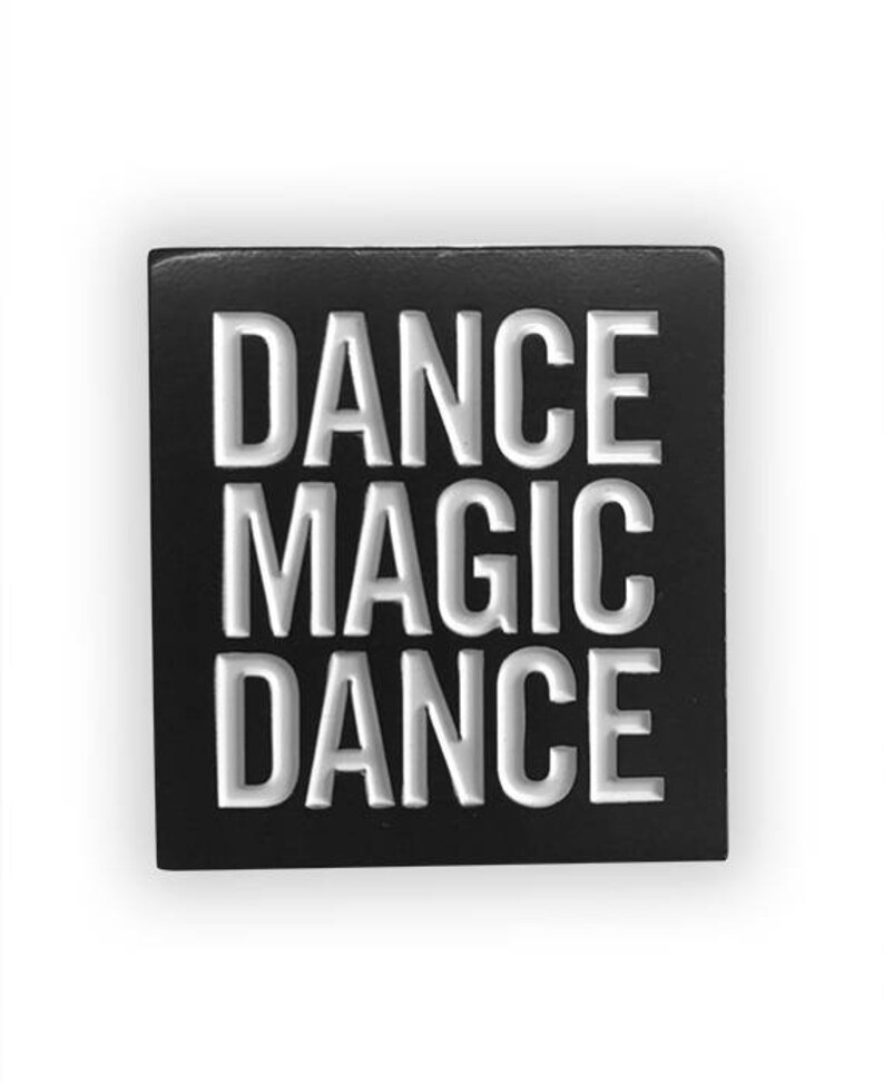 May include: Black square pin with white raised lettering that reads "DANCE MAGIC DANCE".