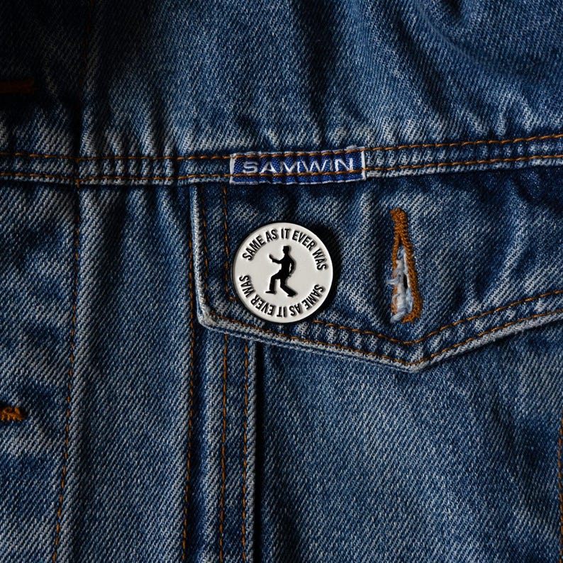 May include: A silver pin with a black silhouette of a person dancing and the text "SAME AS IT EVER WAS" repeated around the edge.