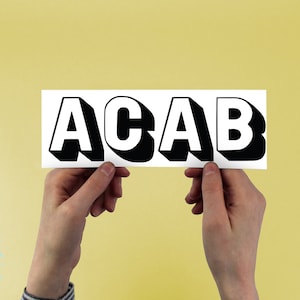 Puede incluir: Una tarjeta blanca con el acrónimo "ACAB" impreso en negro, en letras en 3D. La tarjeta está siendo sostenida por dos manos.