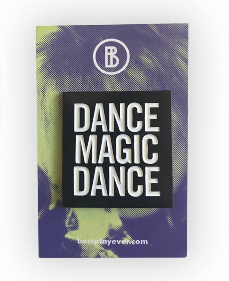 May include: Black enamel pin with white text that reads "DANCE MAGIC DANCE" on a white background. The pin is on a purple and yellow background with a white circle with the letter "B" inside.