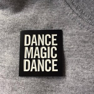 May include: Black square patch with white text that reads "DANCE MAGIC DANCE".