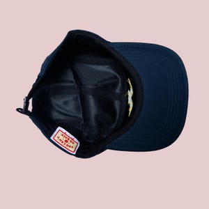 May include: Navy blue baseball cap with a curved brim. The interior features a black mesh lining and a small tag with the text "YOU CAN'T GO BACK". A yellow and white design is visible on the interior.