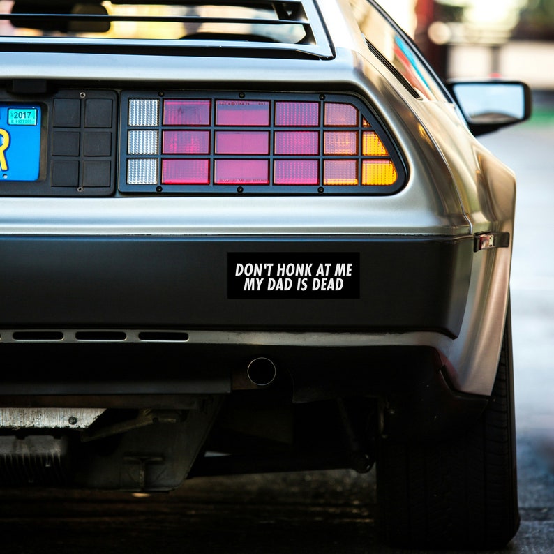 May include: A silver DeLorean time machine with a black bumper sticker that reads "Don't honk at me my dad is dead."