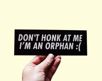 May include: Black and white bumper sticker with the text "DON'T HONK AT ME I'M AN ORPHAN :( "