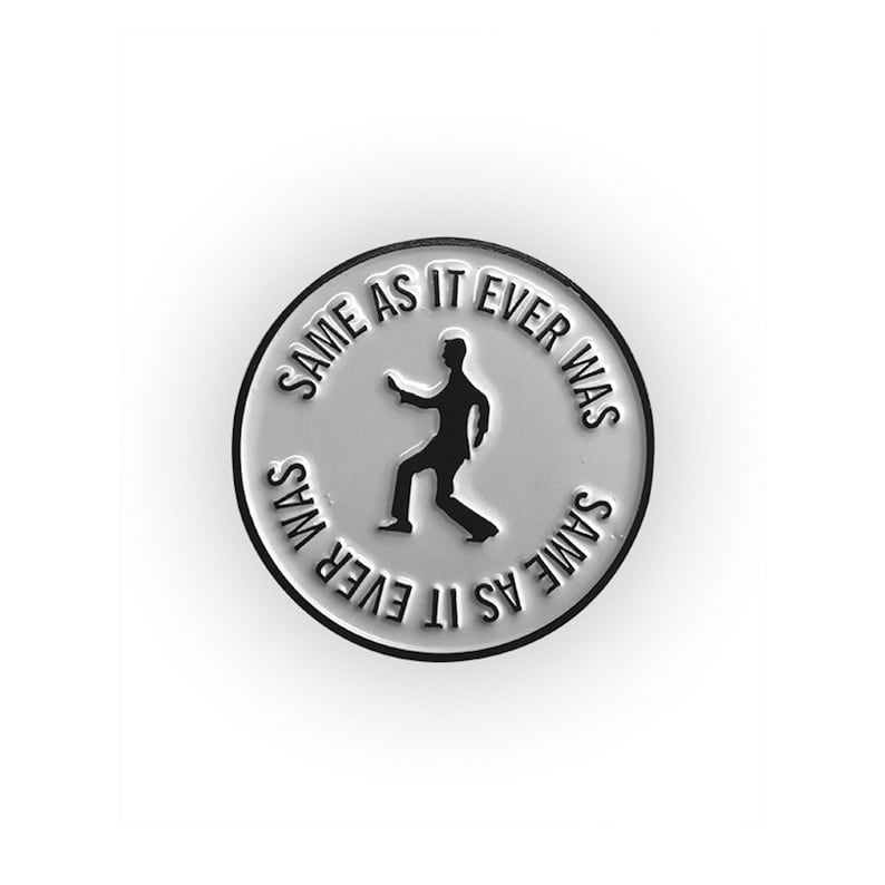 May include: A silver pin with a white background and black text that reads "Same As It Ever Was" around the edge. A black silhouette of a person dancing is in the center of the pin.