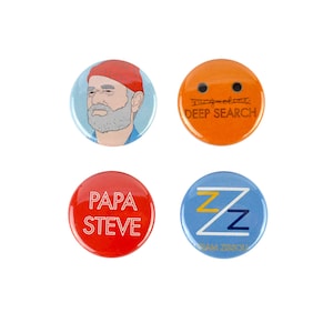 May include: Four round button pins with different designs. The first pin features a cartoon illustration of a man with a red hat and beard. The second pin is orange with the text "DEEP SEARCH" in black. The third pin is red with the text "PAPA STEVE" in white. The fourth pin is blue with a yellow and blue "Z" logo and the text "TEAM ZISSOU" in white.