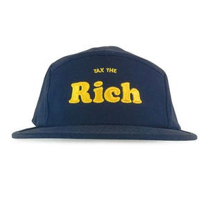 May include: Navy blue cap with the text "TAX THE RICH" embroidered in yellow. The cap has a flat brim and a classic five-panel design, suitable for casual wear.