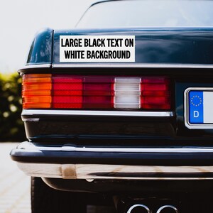 May include: A black car with a white bumper sticker that reads "LARGE BLACK TEXT ON WHITE BACKGROUND".