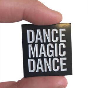May include: Black square sticker with white text that reads "DANCE MAGIC DANCE".