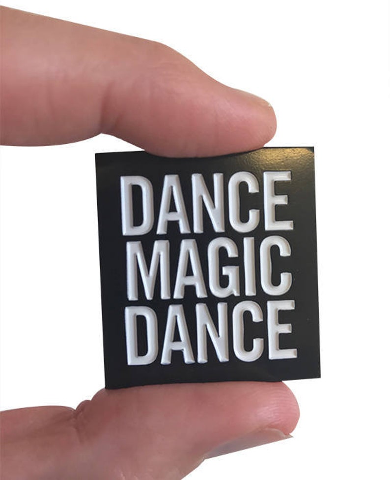 May include: Black square sticker with white text that reads "DANCE MAGIC DANCE".