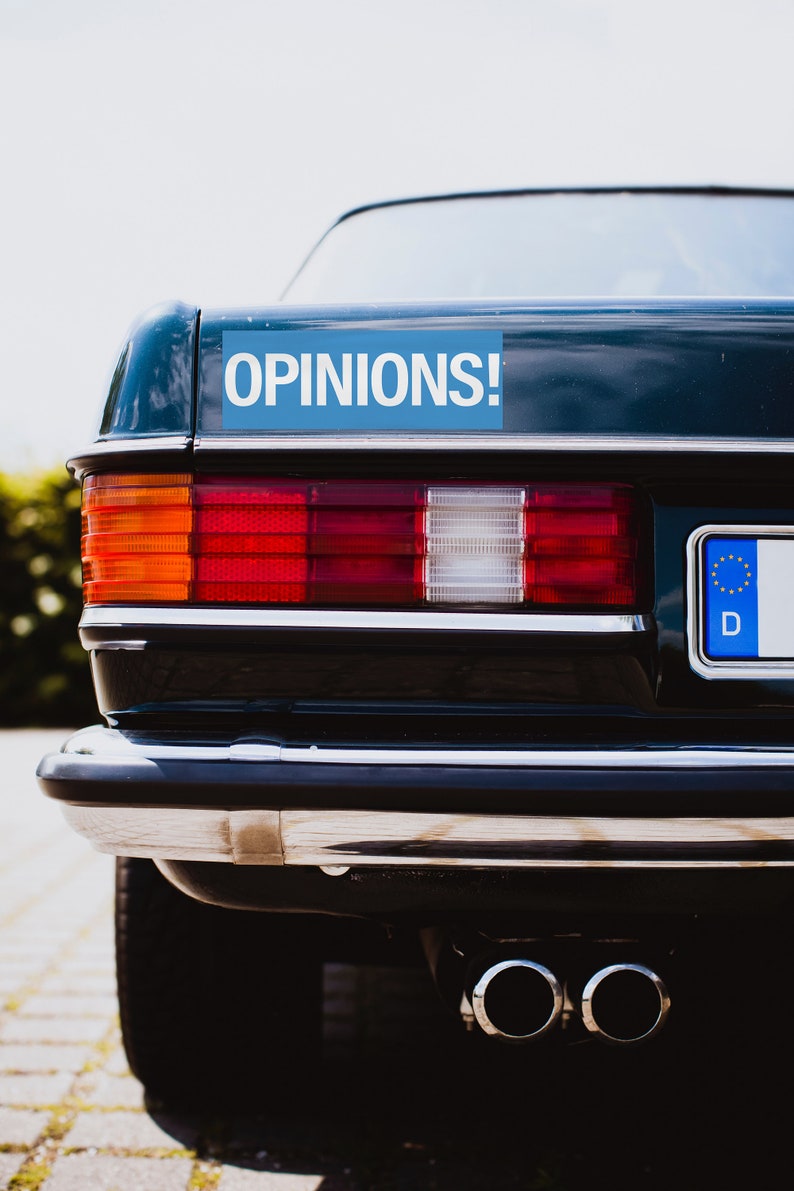 May include: A dark blue car with a blue sticker that says "OPINIONS!" on the back. The car has a European number plate with the letter "D" on it.