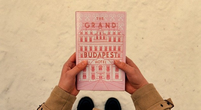 May include: A pink book with the title "The Grand Budapest Hotel" and a drawing of a building on the cover.