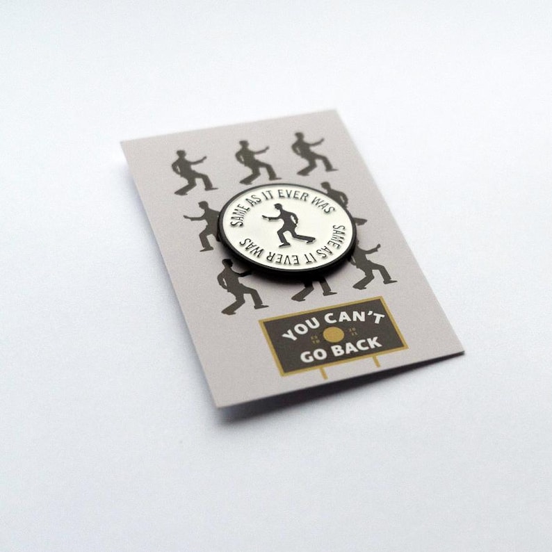 May include: A white enamel pin with a black outline featuring a silhouette of a person dancing with the text "Same as it ever was" written around the edge. The pin is displayed on a card with a black and white illustration of people dancing and the text "You can't go back".