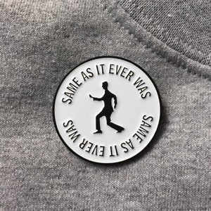 May include: White enamel pin with a black silhouette of a person dancing and the text "Same as it ever was" repeated around the edge.