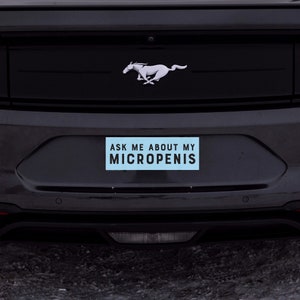 May include: A black car with a silver Mustang logo on the back. A blue bumper sticker with the text "ASK ME ABOUT MY MICROPENIS" is attached to the rear bumper.