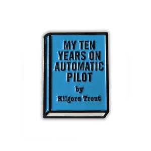 Puede incluir: Un pin de esmalte azul con forma de libro con el título "My Ten Years on Automatic Pilot" de Kilgore Trout.