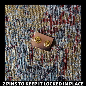May include: A close-up of the back of a gold-colored pin with two metal pins to keep it locked in place.