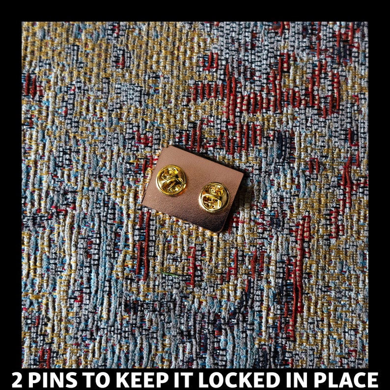 May include: A close-up of the back of a gold-colored pin with two metal pins to keep it locked in place.
