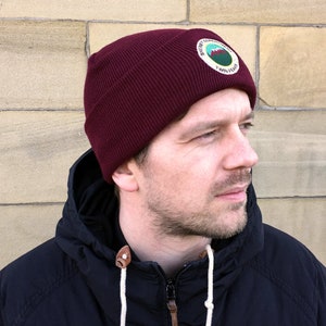 May include: A maroon beanie with a circular patch featuring a green mountain range and the text "SHEEP & GOAT MOUNTAIN" and "TWIN PEAKS".