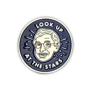 Puede incluir: Un pin de esmalte azul con un contorno blanco de la cara de un hombre y el texto "LOOK UP AT THE STARS".