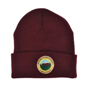 May include: A maroon beanie with a circular embroidered patch that says "Sheriff Department Twin Peaks". The patch features a mountain range and green trees.