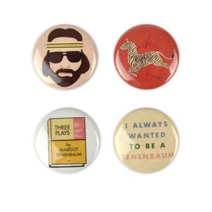 May include: Four circular pin badges with different designs. One shows a cartoon man with sunglasses and a headband. Another features a zebra with arrows on a red background. A third has a book with the text "THREE PLAYS by MARGOT TENENBAUM". The last says "I ALWAYS WANTED TO BE A TENENBAUM".