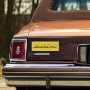 May include: A brown car with a yellow bumper sticker that reads "HONK IF YOU'D RATHER BE WATCHING THE 1999 CINEMATIC MASTERPIECE THE MUMMY STARRING BRENDAN FRASER AND RACHEL WEISZ".