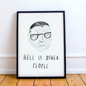 May include: A framed art print with a black border, displaying a sketch of a man wearing glasses. The artwork includes the phrase "HELL IS OTHER PEOPLE" in a handwritten font. The print is set against a white wall and wooden floor.