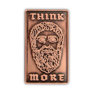 Puede incluir: Un pin de metal de color cobre con una imagen estilizada de la cara de un hombre barbudo y el texto "THINK MORE" en una fuente gótica.