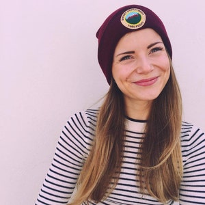 May include: A woman wearing a burgundy beanie with a patch that says "Sheriff Department Twin Peaks". She is wearing a white and black striped shirt.