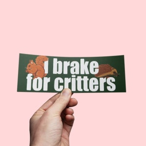 Op de afbeelding: Een donkergroene bumpersticker met de tekst "I brake for critters". De sticker toont illustraties van een eekhoorn en een egel. De tekst is wit.