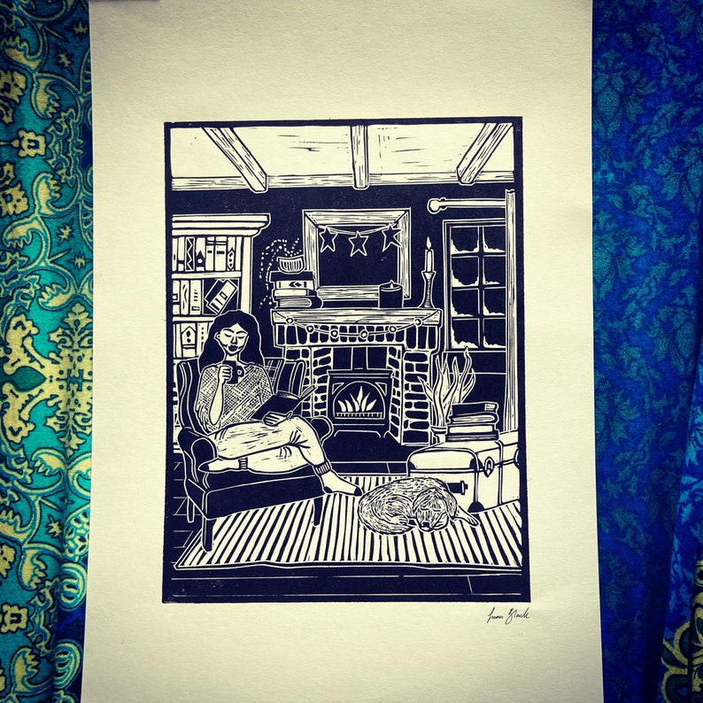 May include: A black and white linocut print of a woman sitting in a chair by a fireplace, reading a book. The fireplace has a fire burning in it and there are books stacked on a shelf to the left of the fireplace. The woman is wearing a long-sleeved shirt and has her hair pulled back. There is a dog sleeping on the floor in front of the fireplace.