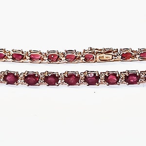 May include: A gold bracelet with a row of oval-shaped red gemstones and smaller diamonds set in the metal.