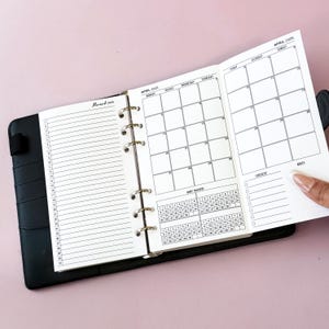 May include: Open black planner with white pages. The left page has a daily schedule, and the right page displays a calendar for April 2020. The planner is open to show the March 2020 and April 2020 calendar pages.