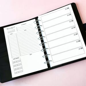 May include: A black disc-bound planner open to a weekly spread. The left page features a January 2028 calendar, top priorities, a to-do list, and habit trackers. The right page displays daily sections from December 28 to January 03 with dot grid paper.