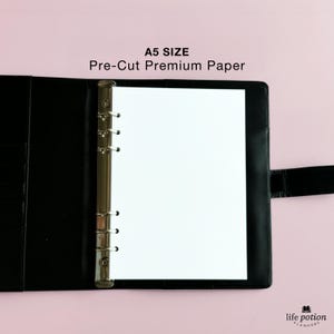 May include: A black binder with a silver ring mechanism is open to reveal a blank white A5 size paper. The text "A5 SIZE Pre-Cut Premium Paper" is printed above the binder.