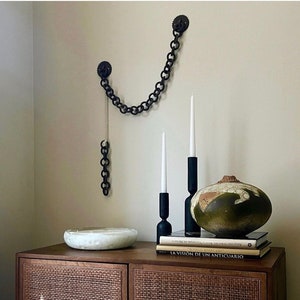 Puede incluir: Un armario de madera con dos puertas y un frente de ratán tejido. El armario está decorado con una cadena, dos candelabros y una calabaza decorativa. El armario está sobre una superficie blanca. El texto "LA VISION DE UN ANTICUARIO" es visible en un libro encima del armario.