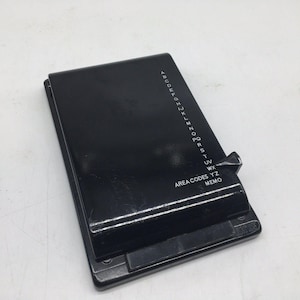 May include: A black address book with a sliding tab and a series of letters down the side. The words "Area Codes YZ Memo" are printed on the front. The book is rectangular and appears to be made of plastic.