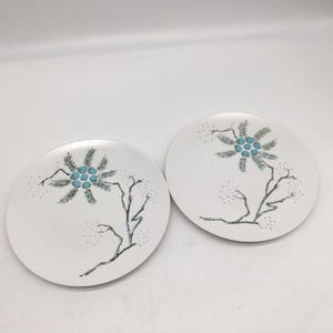 May include: Two white ceramic plates with a botanical design. Each plate features a stylized tree branch with turquoise berries and delicate gray-green leaves. The plates have a simple, elegant aesthetic.