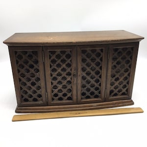 Könnte beinhalten: Ein Holzschrank mit vier Türen und einem Gitterdesign. Der Schrank hat eine mittelbraune Farbe und hat eine gewölbte Oberseite und einen gewölbten Sockel. Ein Holzlineal befindet sich vor dem Schrank.