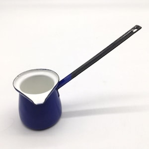 Könnte beinhalten: Eine blaue Emaille-Kaffeekanne mit langem schwarzem Griff. Die Kanne hat einen weißen Innenraum und einen Ausguss zum einfachen Ausgießen. Der Griff hat ein Loch zum Aufhängen. Ein klassischer Küchenartikel.