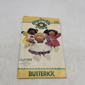 May include: A vintage Butterick pattern for Cabbage Patch Kids clothes. The cover features illustrations of three Cabbage Patch Kids dolls in various outfits. The pattern number is 6509. The cover is yellowed with age.