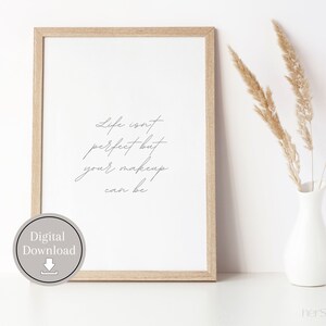 May include: A framed printable with a quote that reads "Life isn't perfect but your makeup can be." The quote is written in a cursive font. The frame is light brown wood and the background is white.