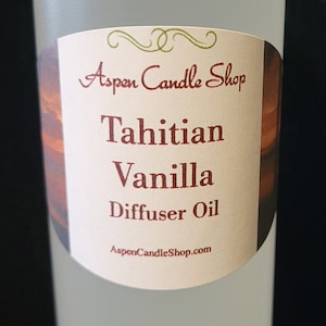 May include: A clear glass bottle with a white cap and a label that reads "Aspen Candle Shop Tahitian Vanilla Diffuser Oil AspenCandleShop.com".