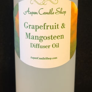 May include: A clear glass bottle with a white cap and a label that reads "Aspen Candle Shop Grapefruit & Mangosteen Diffuser Oil AspenCandleShop.com".