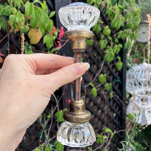May include: A vintage glass door knob with a clear, ribbed design. The knob has brass-colored metal accents and a threaded rod. The overall design is reminiscent of antique hardware.